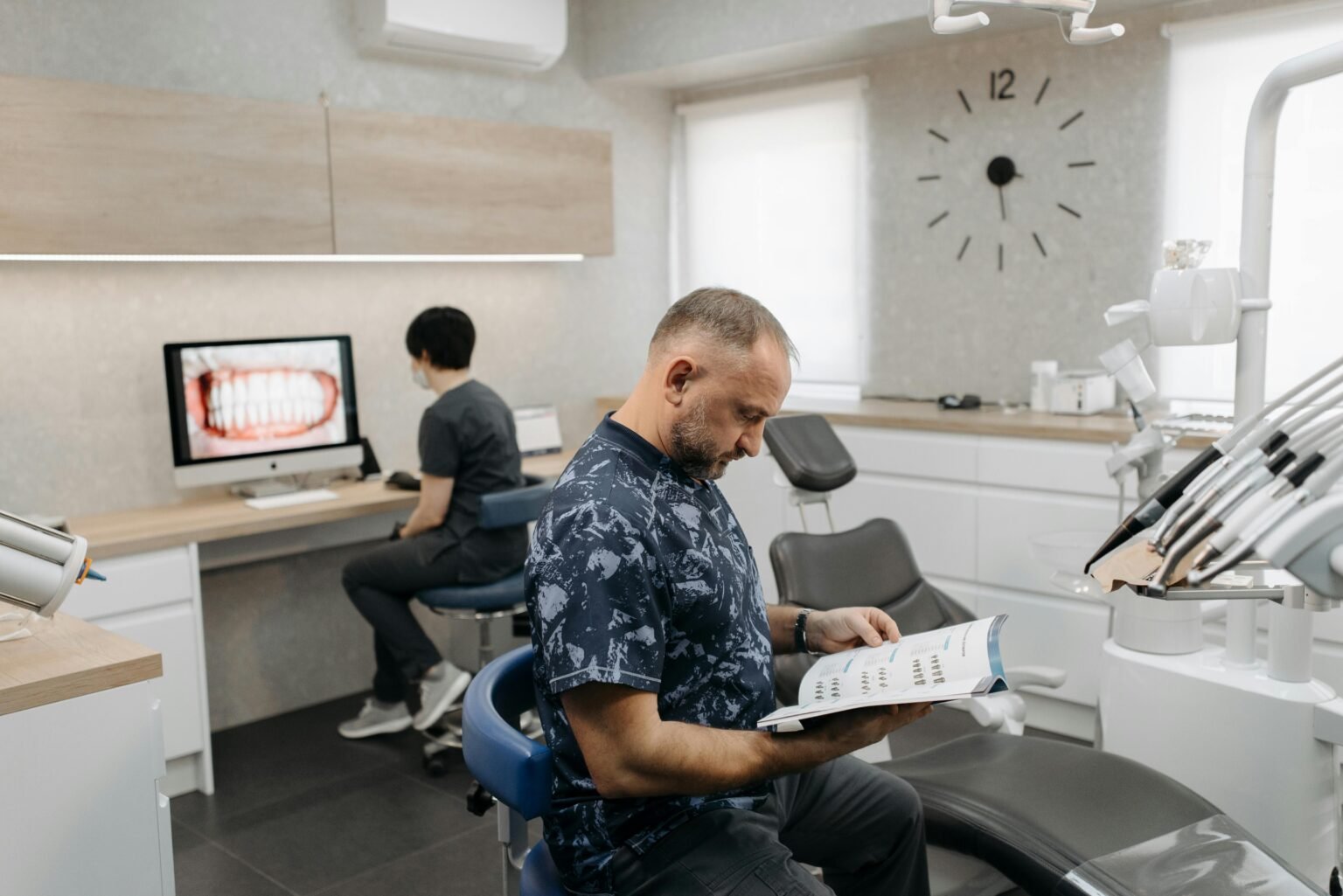 Acasa A dental professional reads a brochure while another works on a computer in a contemporary clinic.